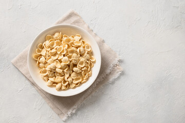 Fresh raw orecchiette pasta made from whole wheat flour in bowl on white background. Copy space. Top view.