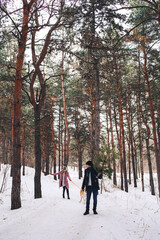 Fototapeta na wymiar Winter walk in the snowy forest. The guy carries the Christmas tree and the girl plays with the dog