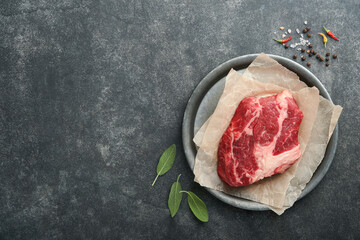 Raw beef steak. Raw fresh Chuck roll steak with rosemary, salt and pepper on cutting board on dark...