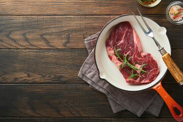 Raw beef steak. Raw fresh Ribeye steak with rosemary, salt and pepper in iron pan on cutting board on dark concrete background. Raw beef steak and spices for cooking.