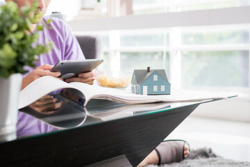 Close up a small wooden house model on a house drawing. Young happy loving couple talking and using...