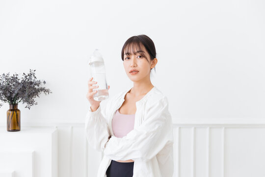 Asian woman with long black hair tied up, wearing sportswear and a white sports jacket. Happy smiling at the camera and holding a water bottle standing on a white background. Image with copy space.