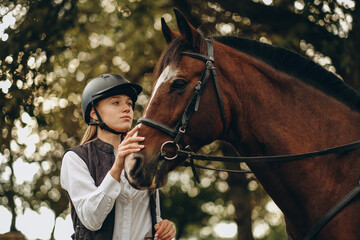 Obraz premium A young female equestrian stands near her horse and prepares for a competition.
