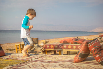 Young Boy Playing at a Colorful Bedouin Camp on the beach  with coffee pots and fire place, jars,...