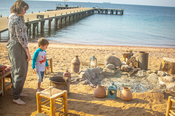 Young Boy Playing at a Colorful Bedouin Camp on the beach  with coffee pots and fire place, jars,...