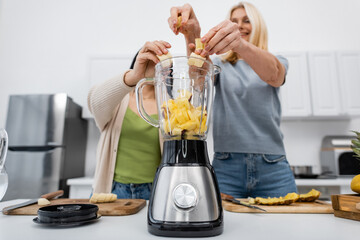 Low angle view of blurred friends putting banana in blender in kitchen