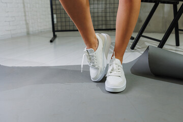 Beautiful woman in youth leather white sneakers and standing on white background. Women's legs with fashionable shoes. Casual white women's shoes