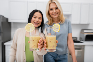 Blurred multiethnic women holding glasses of smoothie at home