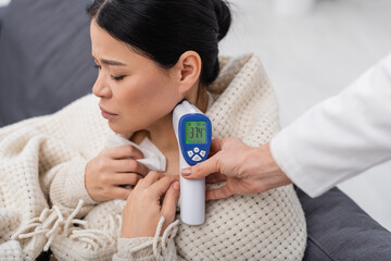 Doctor measuring temperature of sick asian patient at home