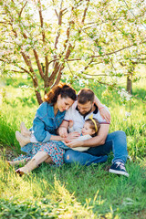 a mom and a dad with a little daughter on a lawn in a blooming spring garden. 