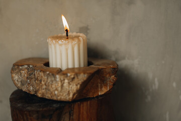 A burning candle in a stone stand. Natural details in the interior. Beige tones
