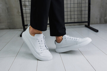 Close-up of male legs in black pants and white casual classic sneakers. Men's summer leather shoes