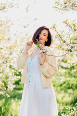 an attractive brunette in a white dress in a blooming spring garden. solar glare