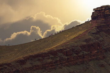 Naklejka premium A group of tourists climbing a hillside at sunset to First Sunduk or Chest butte of a Mountain range Sunduki in Khakassia, Russia mountain range. Traveling in Russia concept