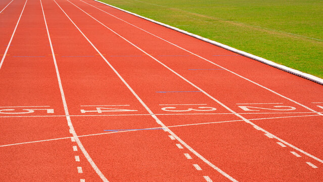 Orange synthetic running racetrack with numbers and greenfield in athletic outdoors stadium