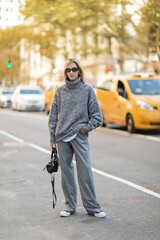 full length of stylish woman in winter outfit standing with trendy handbag near blurred cars in New York