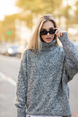portrait of blonde woman in grey sweater adjusting trendy sunglasses on street of New York city