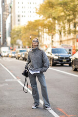 full length of stylish woman in sunglasses and grey outfit holding black handbag and standing on street of New York city