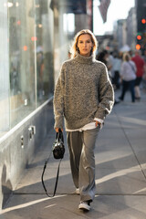full length of young and stylish woman in grey outfit walking with trendy handbag on street of New...