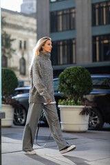 full length of young woman with blonde hair walking in trendy winter outfit in New York