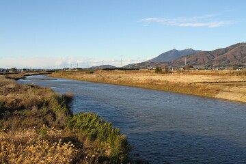 Fototapeta na wymiar Beautiful Japanese Rural Landscape with a River running in front of a Mountains on a Clear Winter Afternoon