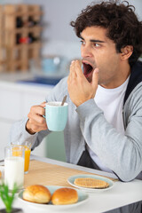 portrait of young man yawning during breakfast