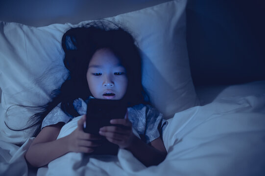 Asian kid playing game on smartphone in the bed at night,The girl Addict social media