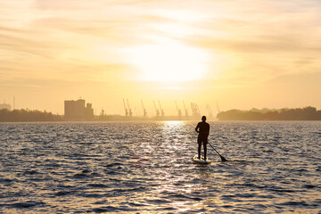 Sporty man standing on stand up paddle board (SUP) at calm Danube river at autumn sunrise