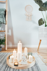 Wooden tray with burning candles and white Buddha statuette on the floor of modern Scandi interior. Zen Composition for meditation, yoga practice, relaxation. Balance and calm energy flow indoor