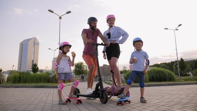 Happy family with kids riding on Segways, electric scooter and skateboards in the Park in the summer, children eating ice cream.