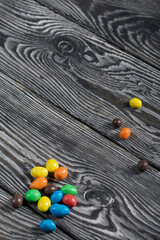 Chocolate candy in multi-colored glaze. Scattered on black pine boards.