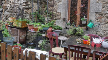 Une ruelle artisanale et jardinage, avec plusieurs petits pots, beaucoup de fleurs, décoration extérieur avec animaux, stands, sol mouillé, temps de pluie, maisons en pierres, entretien jardin