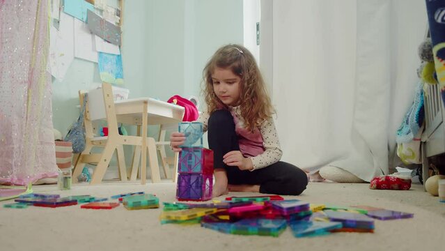 Toddler girl building a tower with magnetic tiles. Home learning. STEM concept. 4K cinematic.