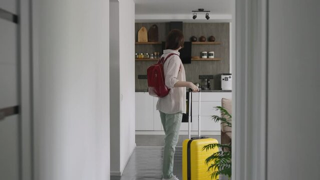 A young pleasant woman moves into a rented apartment. The tourist arrived with a yellow suitcase and backpack.