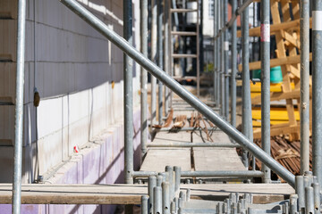 Detail einer großen Baustelle: Blick auf das Gerüst seitlich an einer bereits errichteten Steinmauer eine Gebäudes mit Absperrungen, Sicherungen, Planken, Leitern, Material, Werkzeug und Streben