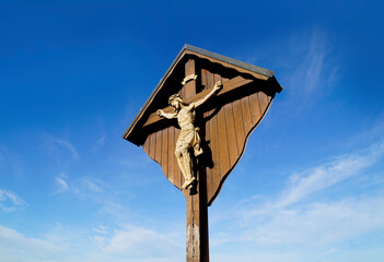 a footpath in the fields overlooking a wooden cross with Jesus Christ in the Bavarian village Konradshofen on a sunny on a Christmas day (Germany)