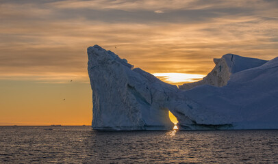 Eisberg in Grönland mit Loch im Sonnenuntergang