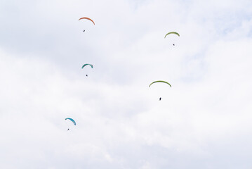 Five paragliders flying  on a cloudy day.