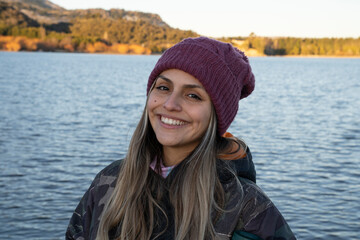 Portrait of a young woman smiling. The placid lake and mountains in the background.