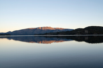 View of the calm lake and mountains at sunset. Beautiful landscape and sky reflection in the water surface. 
