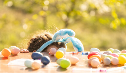 Fototapeta na wymiar cute teenage girl wearing bunny ears and holding Easter eggs against the garden