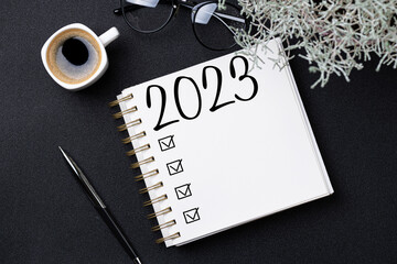 New year resolutions 2023 on desk. 2023 resolutions list with notebook, coffee cup on black...
