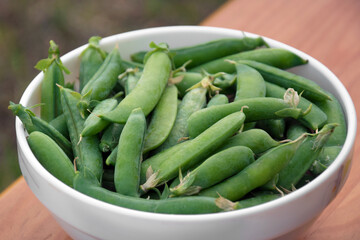 Green peas in a white plate on a wooden bench.