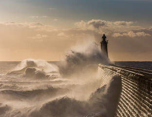 Big waves batter the lighthouse & north pier guarding the mouth of the Tyne in Tynemouth at sunrise, England
