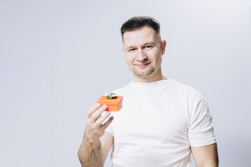 A man in a white t-shirt holds a birthday and valentine's day gift in his hand