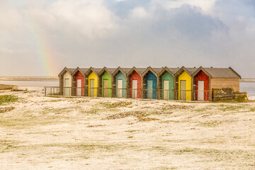 The colorful beach huts at Blyth beach surrounded by snow and with a rainbow overhead in a wintery Northumberland, England