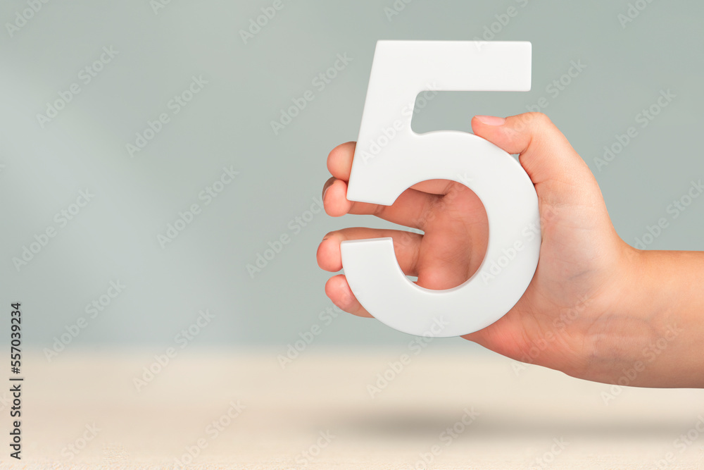 Fototapete Number five in hand. Hand holding white number 5 on blurred background with copy space. Concept with number five. Birthday 5 years, fifth grade, five day work week