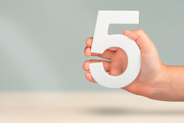 Number five in hand. Hand holding white number 5 on blurred background with copy space. Concept...