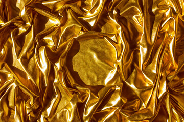Golden wavy abstract background from a luxurious fabric, wavy folds, in the center a place for your gift in the form of a circle.