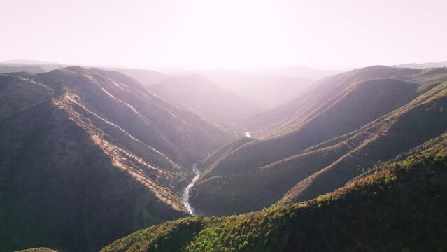 Sideways moving aerial shot over epic mountain and valleys during sunrise. River runs far below.